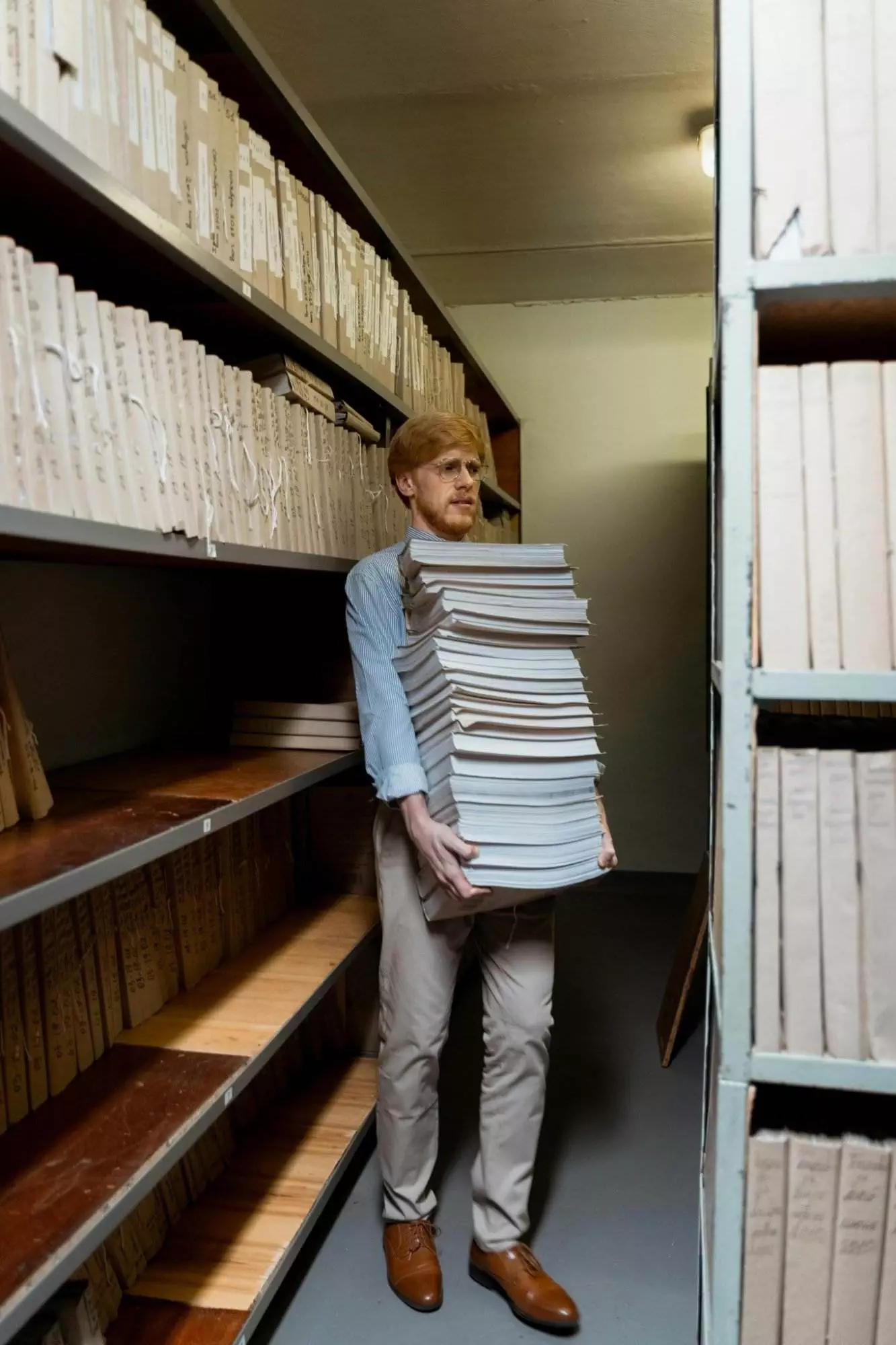 Erwachsener Mann in einem Archivraum mit einem großen Stapel von Dokumenten, umgeben von Regalen. Dokumenten Archivierung ohne DMS